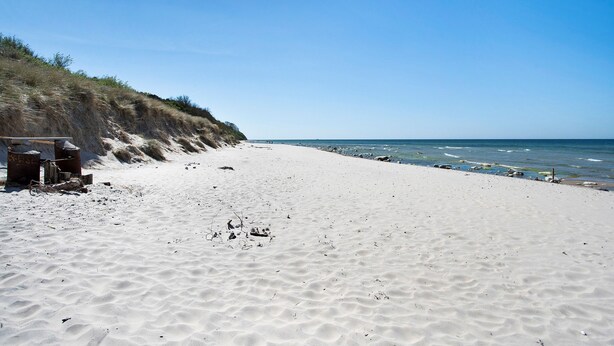 Una spiaggia sabbiosa con cielo sereno, una scogliera rocciosa e l'oceano.