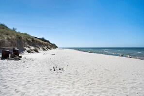 A sandy beach with a clear sky, a rocky cliff, and the ocean.