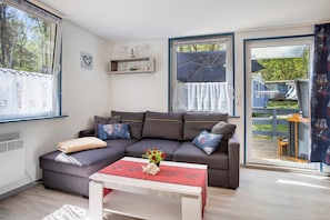 A modern living room with a grey sofa, a white coffee table, and a window with a view of the outdoors.