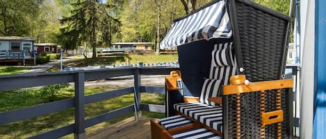 A wooden deck with a bed featuring a striped canopy and a small table.