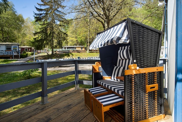 A wooden deck with a bed featuring a striped canopy and a small table.