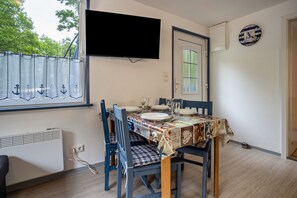 A dining area with a table set for four, a TV mounted on the wall, and a window with curtains.