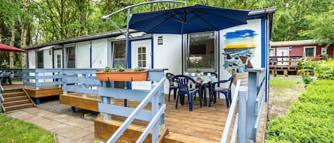 Een houten terras met buitenmeubilair, een overdekt gedeelte met een parasol, en een gebouw met een muurschildering.