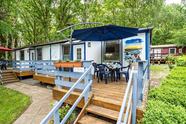 A wooden deck with outdoor seating, a covered area with an umbrella, and a building with a mural.