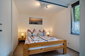 A bedroom with a wooden bed, two bedside tables, a nightstand, a window with curtains, and a wall-mounted lamp.