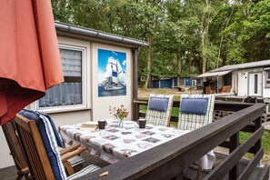 A wooden deck with a table, chairs, and a small table with a vase and two cups. - Bungalow 'Bungalow Schoner Greif, Bgl 8' with Private Terrace and Wi-Fi (Dranske)