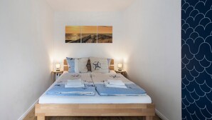 Un dormitorio con cama de madera, dos mesitas de noche con lámparas, una obra de arte en la pared que representa un atardecer y una cortina estampada.