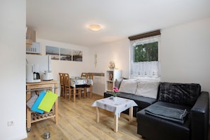 A compact living space with a dining area, a sofa, and a small table with a decorative item. - Bungalow 'Bungalow Schoner Greif, Bgl 8' with Private Terrace and Wi-Fi (Dranske)