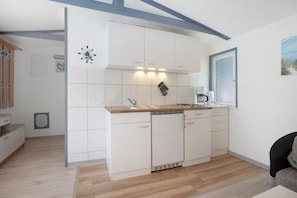 A compact kitchen with white cabinets, a wooden countertop, a built-in dishwasher, and a window with a view.