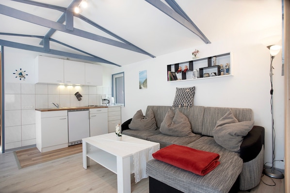 A modern living space with a kitchen, white furniture, and a grey sofa with a red throw.