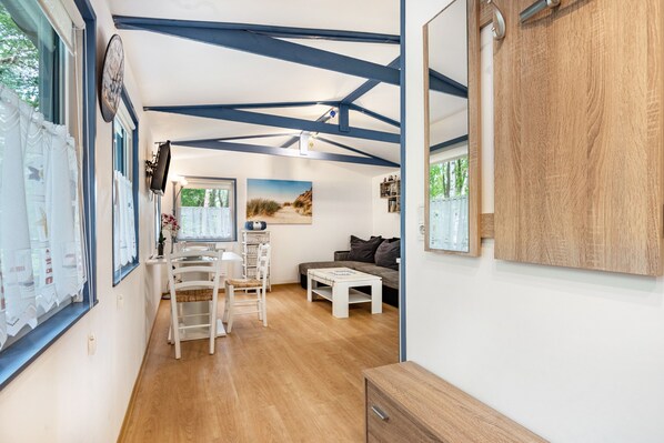 A room with a wooden floor, a white dining table with chairs, a sofa, a wooden cabinet, and a large mirror.