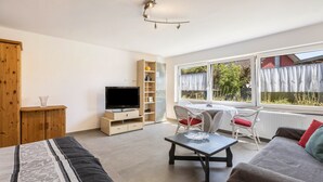 Een moderne kamer met een bed, een televisie, een bureau en een raam met uitzicht op groen.