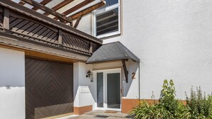 Een huis met een houten veranda, een garagepoort, een deur met ruitpanelen en een kleine tuin met planten.