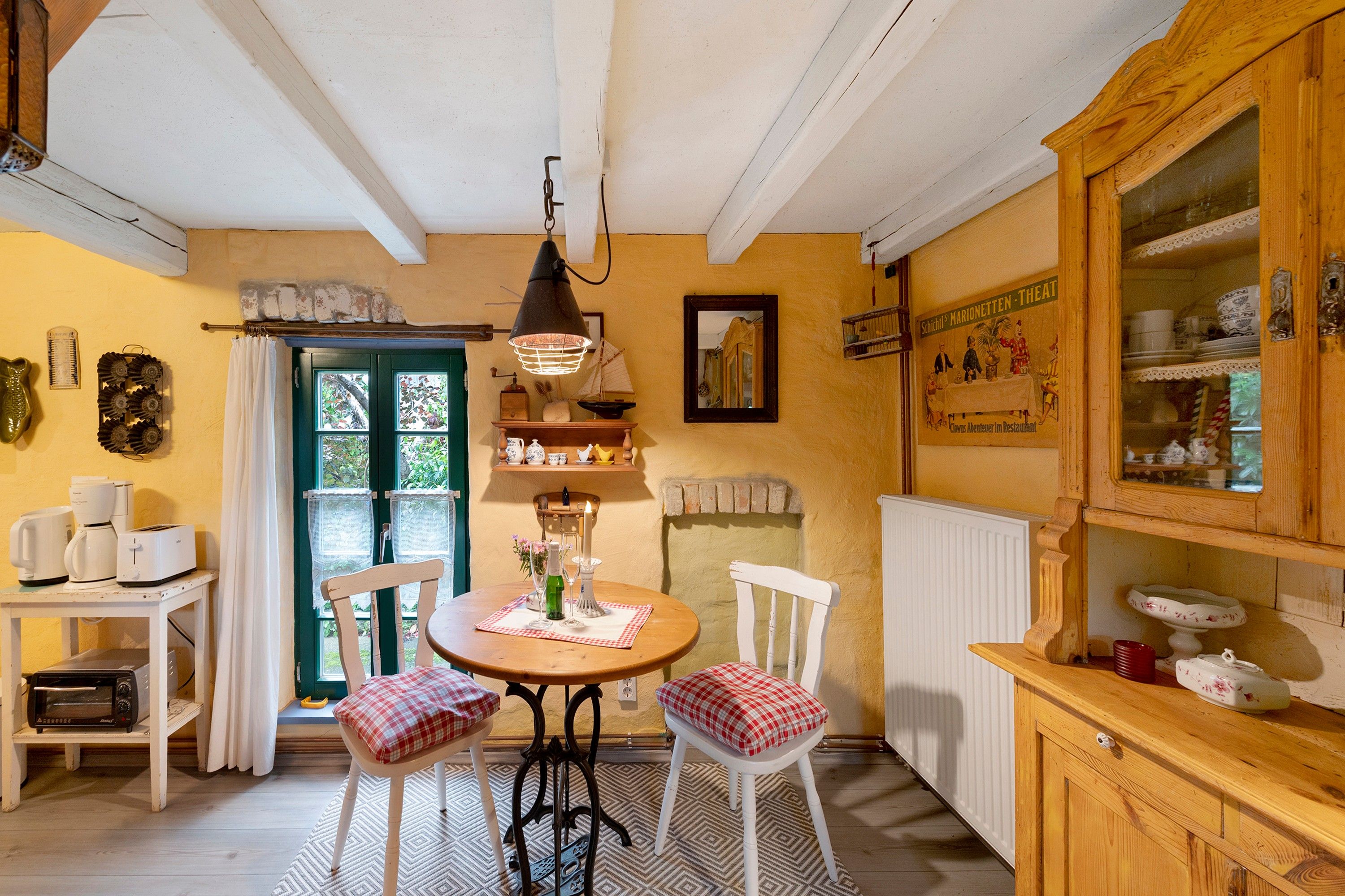 Une cuisine chaleureuse avec une table à manger, des chaises, un luminaire suspendu et un buffet en bois contenant de la vaisselle.