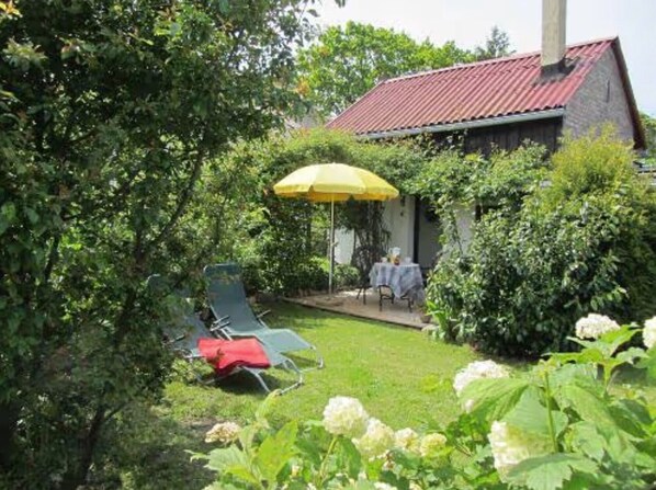 Una casa con tetto rosso, un patio con ombrellone giallo e un giardino con fiori bianchi.