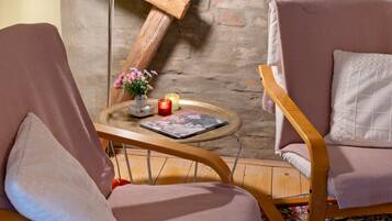 A cozy room with two armchairs, a small table with a book and candles, and a rustic brick wall.
