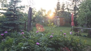 A garden with various plants and flowers, a wooden structure, and tall trees. - Holiday Home 'Villa Ilsebill' with Private Terrace and Garden (Ribnitz-Damgarten)