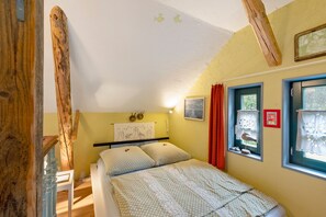 Quarto com cama, janela com cortinas, quadro pendurado na parede e estrutura de vigas de madeira.
