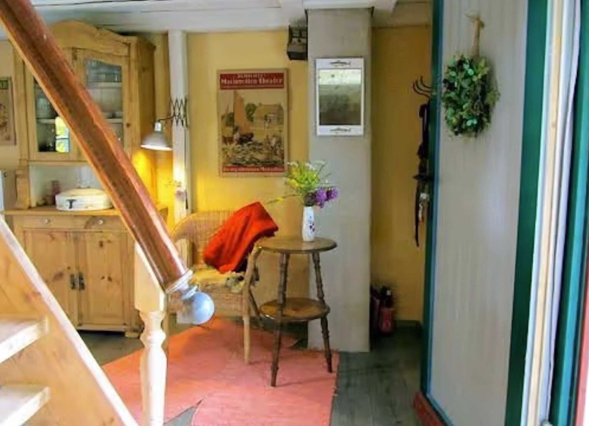 A wooden staircase leading to a kitchen with cabinets, a dining table with a vase of flowers, and a wall-mounted sign.