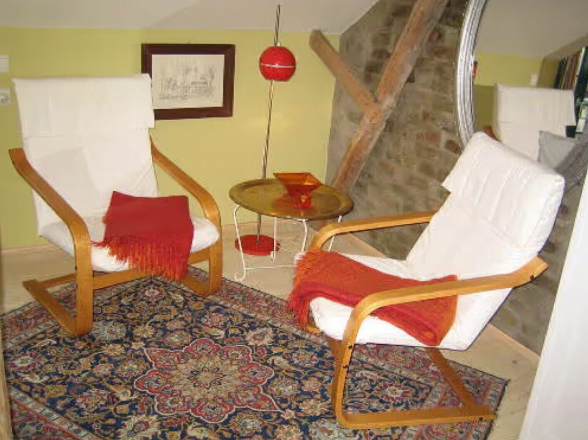 A room with two wooden chairs, a patterned rug, a small round table, and a framed picture on the wall.