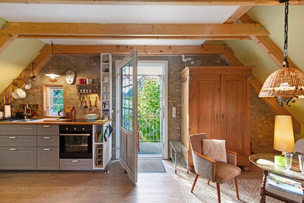 A kitchen with a wooden ceiling, a dining area with a chair and table, and a view of the outside.