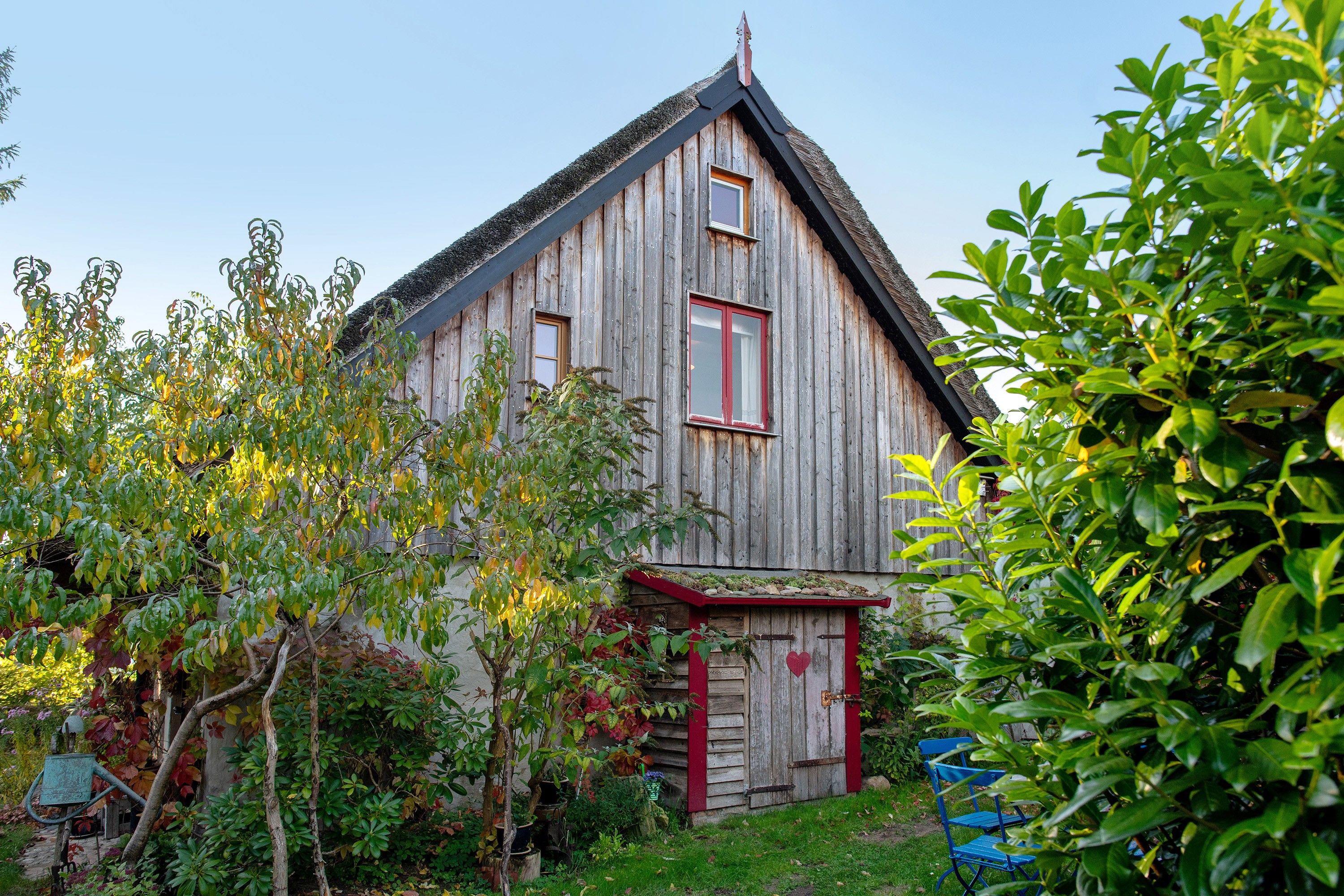 A rustic wooden house with a steeply pitched roof, a red door, and a small porch.