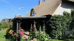 Ein Haus mit Strohdach, einer Veranda und einem Blumengarten.