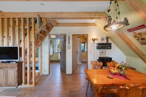 A spacious room with a wooden staircase, a dining area with a table set for two, and a television on a cabinet.