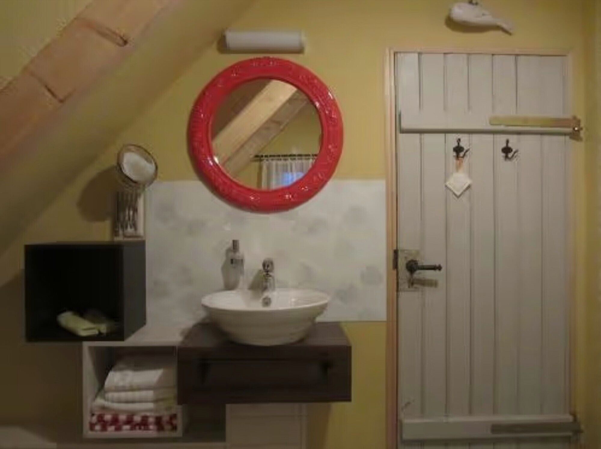 Un bagno con un lavandino bianco, uno specchio con cornice rossa, un portasciugamani e una porta con un asciugamano appeso.