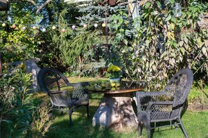 An outdoor seating area with wicker chairs and a round table, surrounded by lush greenery and a variety of plants.