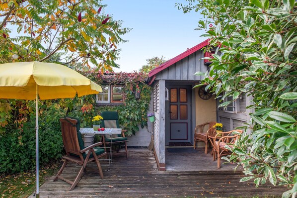 A wooden deck with outdoor furniture, a covered table, and a small building with a red roof.