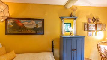 A room with a bed, a blue cabinet, a painting, and a wicker chair.
