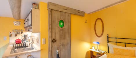 A room with a bed, a nightstand, a wall clock, a mirror, and a wooden door.