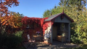 A small cabin with a red roof, a wooden table, and two chairs outside. - Holiday Home 'Charlottes Landlust' with Private Terrace and Garden (Ribnitz-Damgarten)