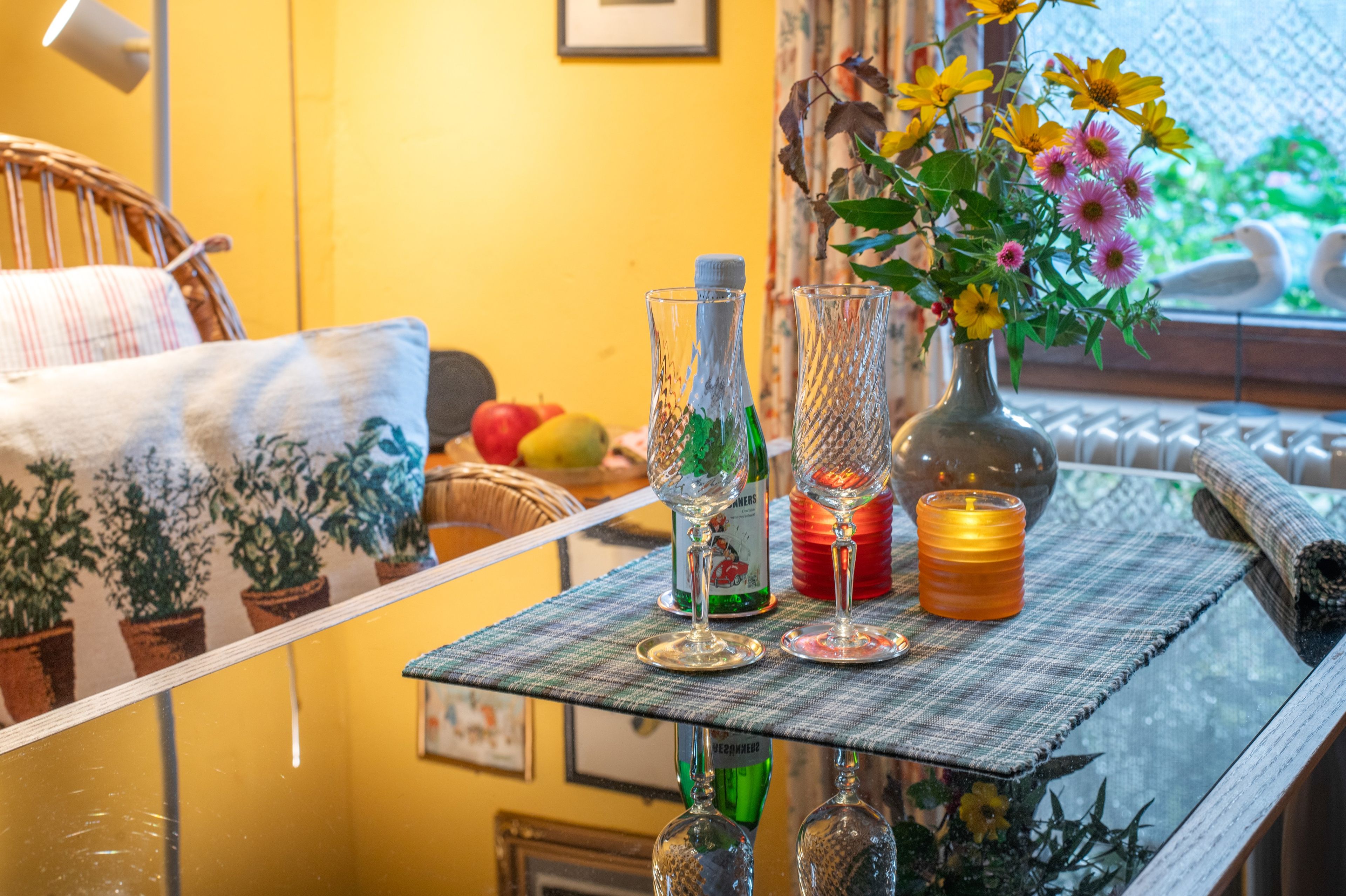 Una mesa de cristal con objetos decorativos, incluyendo una botella, una vela y un florero con flores.
