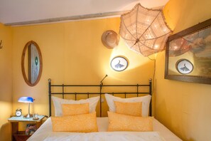 A bed with two pillows, a bedside table with a lamp, and a wall with a mirror and framed pictures.