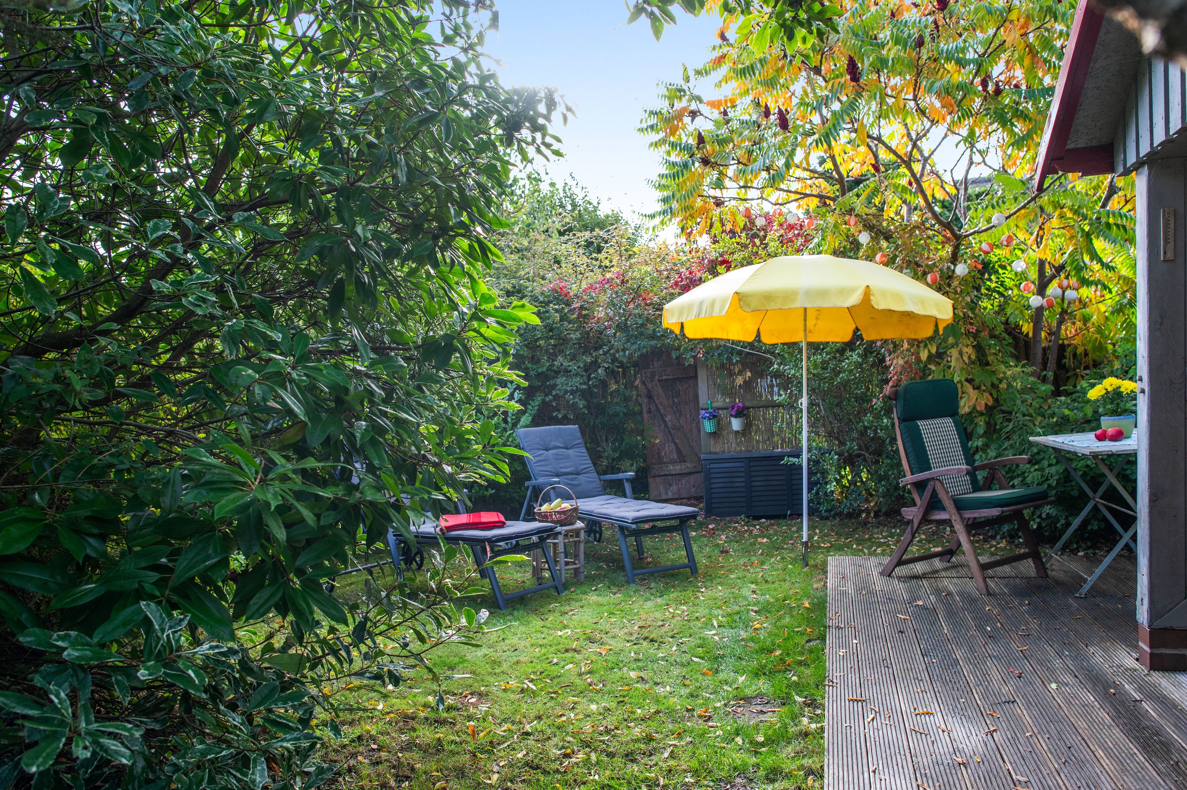 Eine Terrassenfläche mit einem gelben Sonnenschirm, zwei Liegestühlen und einem kleinen Tisch.