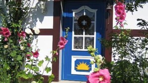 A house with a blue door, a wreath, and pink flowers. - Holiday Home 'Charlottes Landlust' with Private Terrace and Garden (Ribnitz-Damgarten)
