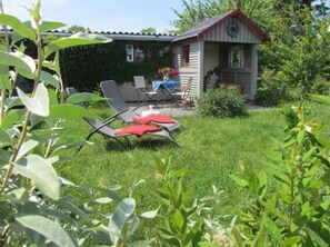 Een klein huis met een tuin, zitplaatsen buiten en een klok aan de muur.