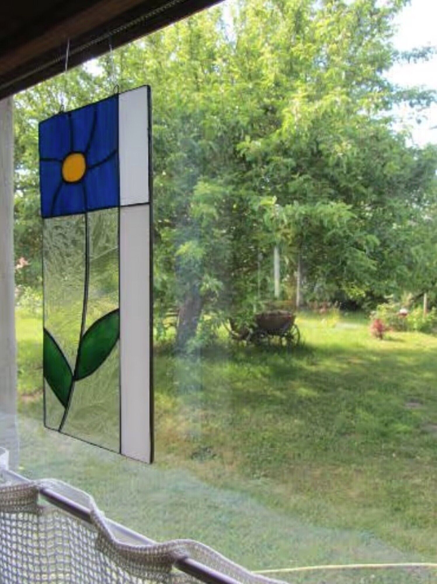 Ein Fenster mit einem farbigen Glasdekor, Blick auf einen grünen Garten und einen Baum.