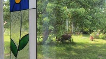 Ein Fenster mit einem farbigen Glasdekor, Blick auf einen grünen Garten und einen Baum.