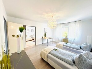 Habitación de hotel moderna con una cama grande, un sofá, una mesa de comedor y vistas al exterior.
