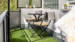 Un petit espace extérieur aménagé avec une table et des chaises, un pot de fleurs et une vue sur l’extérieur.