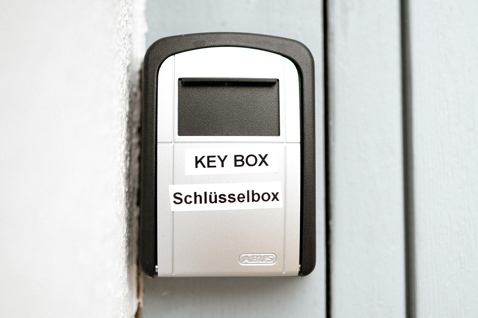 Une boîte à clés portant les inscriptions « KEY BOX » et « Schlüsselbox », fixée à une porte.