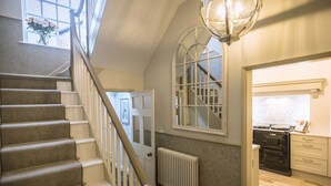 Un escalier avec une rampe menant à un palier, un radiateur en dessous, et un coin cuisine avec des placards et une cuisinière.
