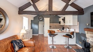 A modern living room with a leather sofa, a wooden-framed ceiling, a kitchen with white cabinets, and a fireplace. - Sun Hill Palins -  a cottage that sleeps 2 guests  in 1 bedroom (Leyburn)