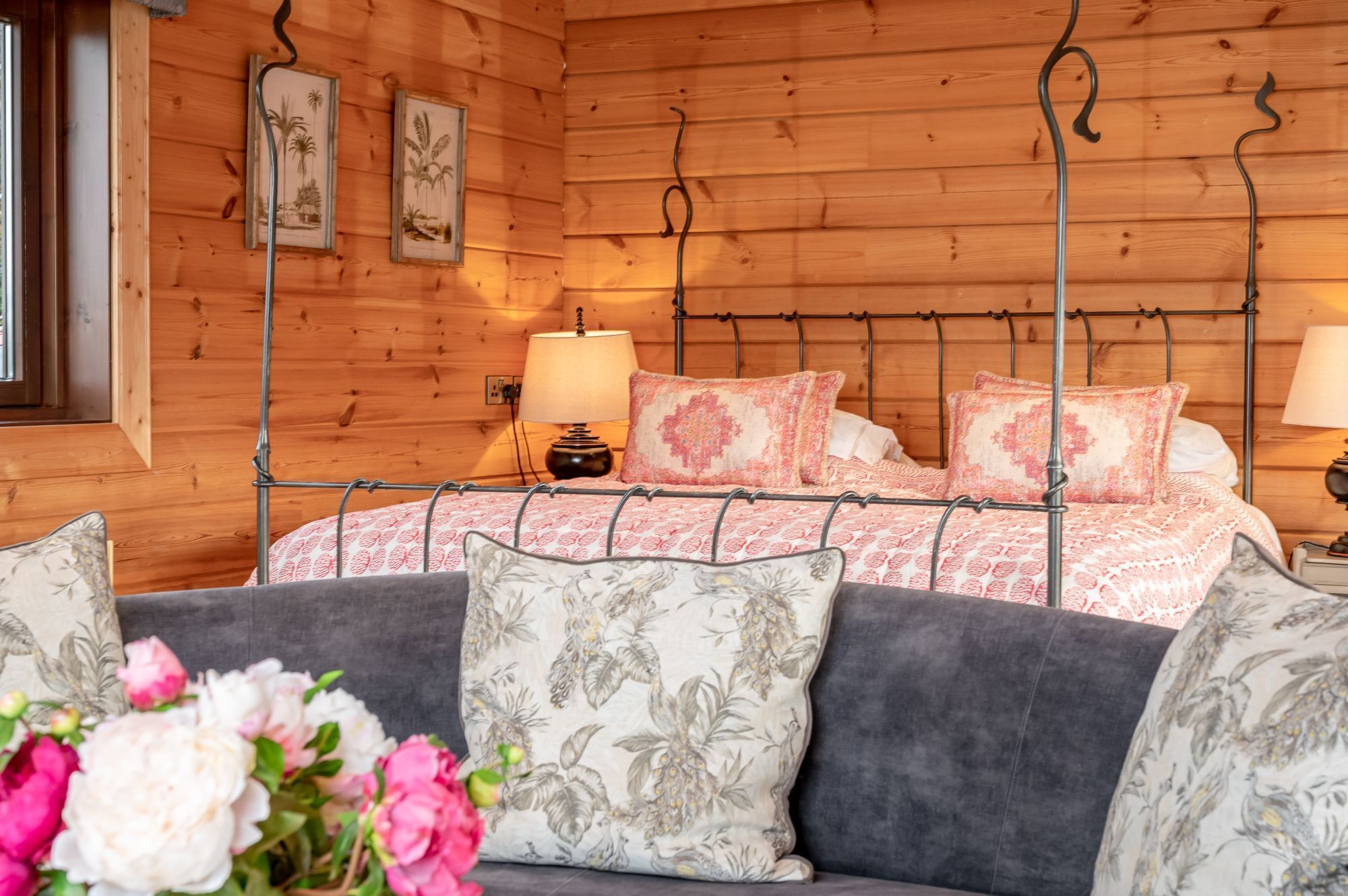 Ein Schlafzimmer in einer Holzhütte mit einem Metallbettgestell, Kissen mit Blumenmuster und einem Nachttisch mit Lampe.