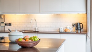 A kitchen with white cabinets, a white tiled backsplash, a bowl of fruit on the counter, a kettle, and a coffee pot. - Abbey -  a lodge that sleeps 6 guests  in 3 bedrooms (Richmond)