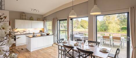 Spacious open-plan kitchen and dining area at Abbey, featuring a central island, built-in oven, and large sliding doors opening onto the lakeside deck for outdoor dining.
