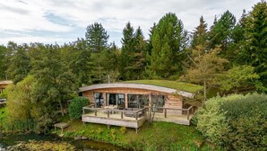 A modern house with a curved roof, large windows, and a deck overlooking a pond with lily pads. - Abbey -  a lodge that sleeps 6 guests  in 3 bedrooms (Richmond)